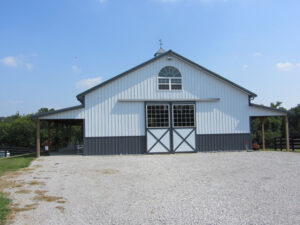 Large, post-frame white equestrian barn on clear day.