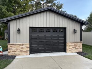 Residential Post Frame Construction garage with brick base, black door and beige trim