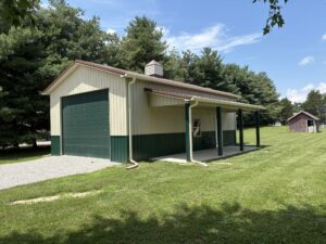 Residential post-frame construction garage with green door, yellow trim, and side porch